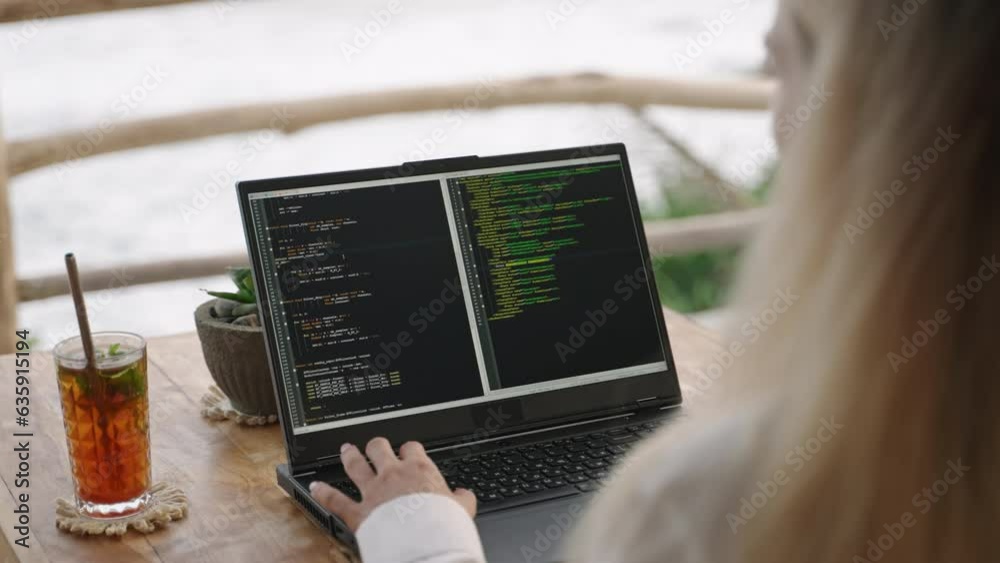 Female soft dev with laptop on remote work day in tropical cafe. Software developer writes program code on computer screen in coworking restaurant with sea view on sunset. Woman coding by ocean.