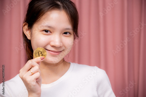 Portrait of a smiling Asian woman wear white shirt and holding banknotes or money us dollar and bitcoin BTC included with Cryptocurrency hand picked on pink background.