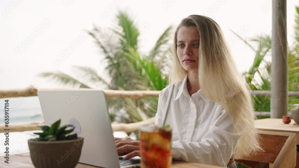 Pretty woman working with laptop in cafe with ocean view, palm trees. Female typing on computer keyboard sitting in tropical restaurant. Business person on remote work day. Nice girl drinks cold tea. Pretty woman working with laptop in cafe with ocean view, palm trees. Female typing on computer keyboard sitting in tropical restaurant. Business person on remote work day. Nice girl drinks cold tea.