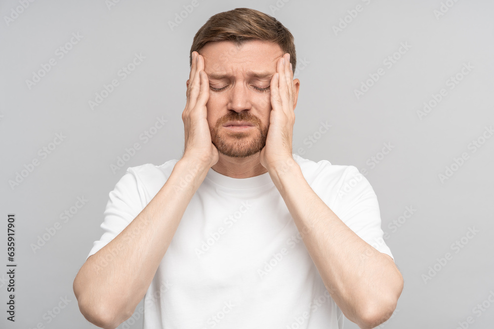 Tired man holds his head suffering from pain. Middle aged male suffers from terrible pain in head. Headache, migraine, overwork, illness, stress. Isolated on studio gray background Tired man holds his head suffering from pain. Middle aged male suffers from terrible pain in head. Headache, migraine, overwork, illness, stress. Isolated on studio gray background