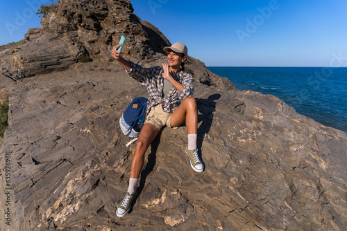 tourist girl with a backpack in the summer on top of a mountain takes a selfie against the backdrop of the sea and mountains