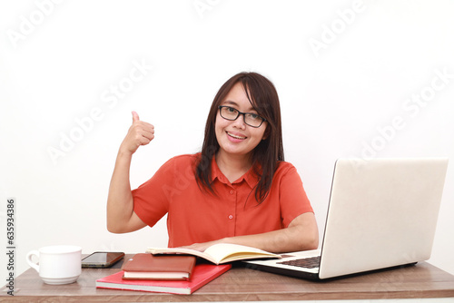 Happy young asian entrepreneur woman sitting while showing thumbs up. Isolated on white