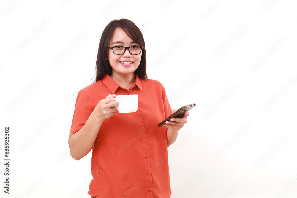 Naklejka premium Portrait of happy young asian woman standing while holding cell phone and a cup of coffee