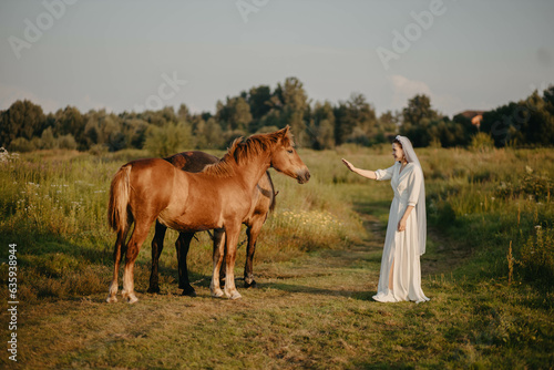 woman bride in white dress in field with horses on wedding day