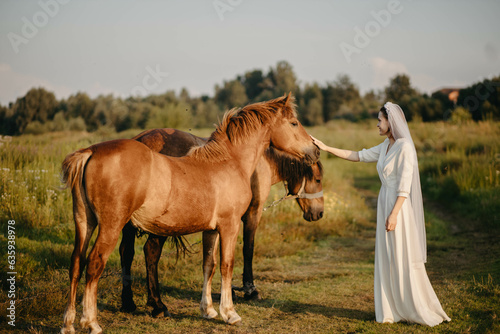 woman bride in white dress in field with horses on wedding day