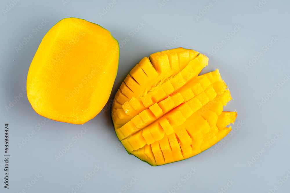 Cut and Uncut Cored Mango Halves on a Blue Background: Half of a mango that is diced with the other half uncut Cut and Uncut Cored Mango Halves on a Blue Background: Half of a mango that is diced with the other half uncut