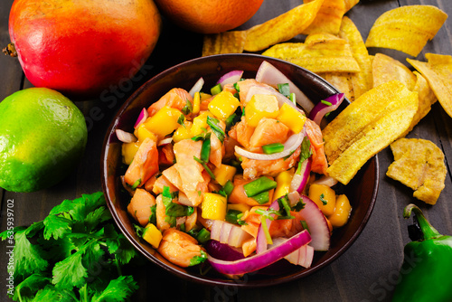 Salmon Ceviche with Mango in a Wooden Bowl with Plantain Chips: A bowl of salmon ceviche with plantain chips surrounded with ingredients