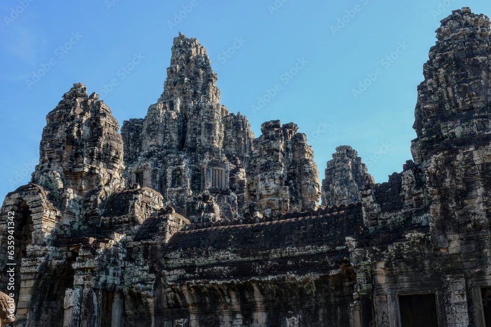 General view of the ancient Bayon Temple with stone towers and human faces in Cambodia on a sunny day.