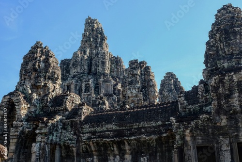 General view of the ancient Bayon Temple with stone towers and human faces in Cambodia on a sunny day.