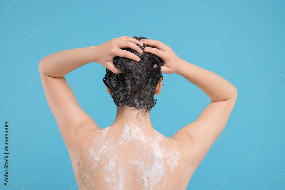 Woman washing hair on light blue background, back view
