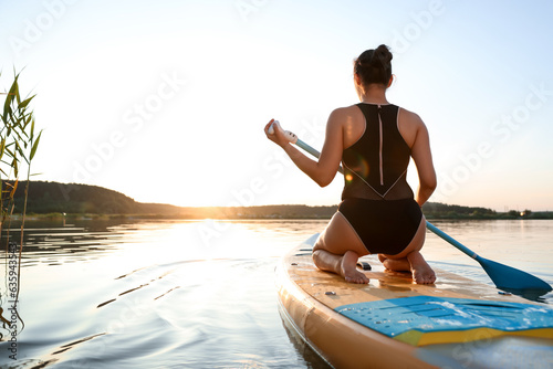 Valokuva Woman paddle boarding on SUP board in river at sunset, back view