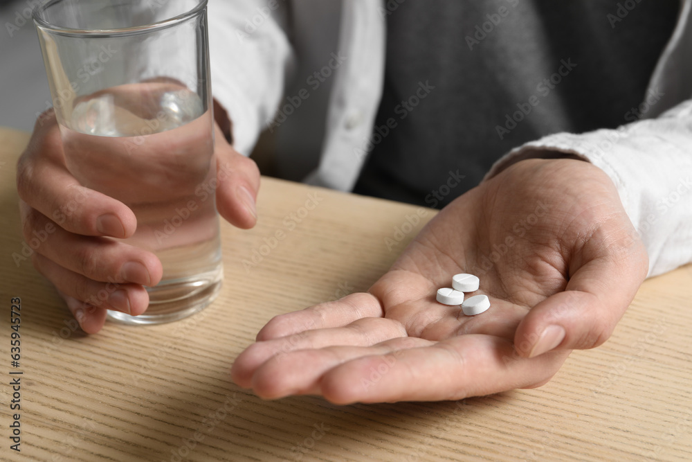 Man with glass of water and pills at wooden table, closeup Man with glass of water and pills at wooden table, closeup