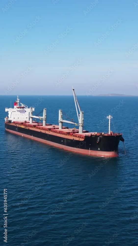 Bulk cargo carrier sea ship anchored in Aegean sea waiting entering port, Aerial vertical social media Bulk cargo carrier sea ship anchored in Aegean sea waiting entering port, Aerial vertical social media