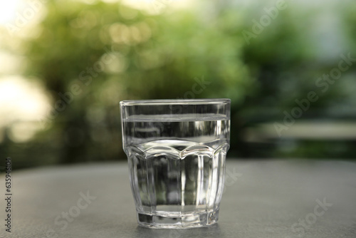 Glass of fresh water on grey table outdoors, closeup