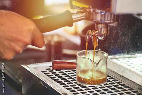 Man's hand operating a coffee machine And there is water from the coffee beans flowing from the coffee maker down to the glass.