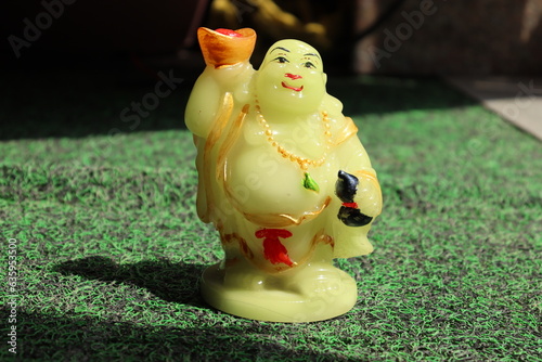  Statue of Laughing Budha made up of yellow Marble holding a bowl on a grass carpet, Vastu or Feng sui item photo