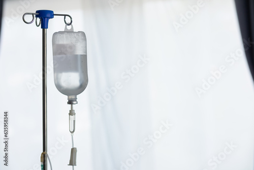 фотографія An iron stand to hang saline bottle high to deliver saline via catheter to an intravenous patient lying on patient bed