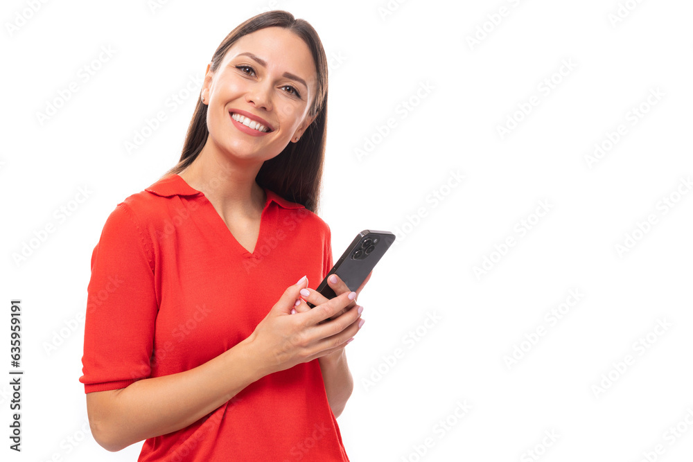 young cute kind european woman with black hair is dressed in a red t-shirt with a smartphone on a white background young cute kind european woman with black hair is dressed in a red t-shirt with a smartphone on a white background