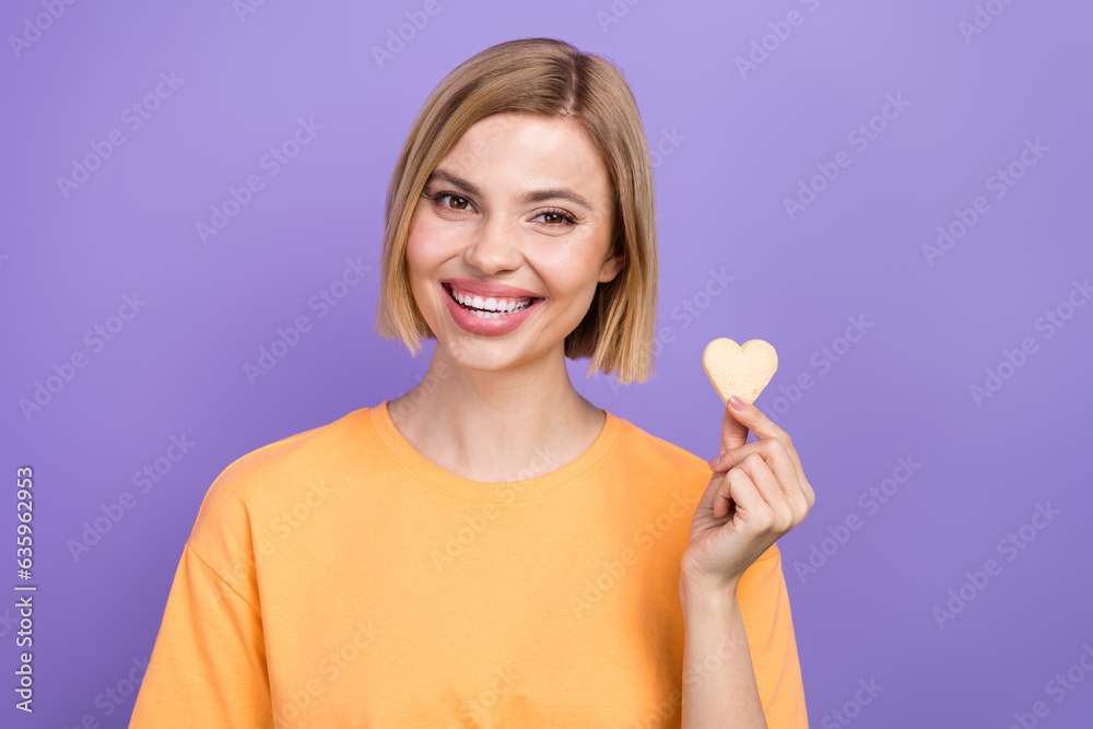 Photo of attractive young woman blonde bob hair wear yellow t shirt holding baked sweet cookie dessert isolated on violet color background Photo of attractive young woman blonde bob hair wear yellow t shirt holding baked sweet cookie dessert isolated on violet color background