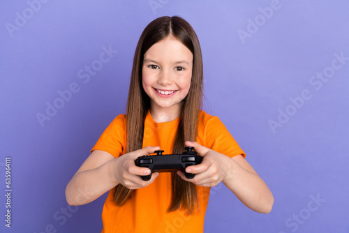 Portrait of satisfied schoolgirl with long hair wear stylish t-shirt hold playstation joystick isolated on violet color background