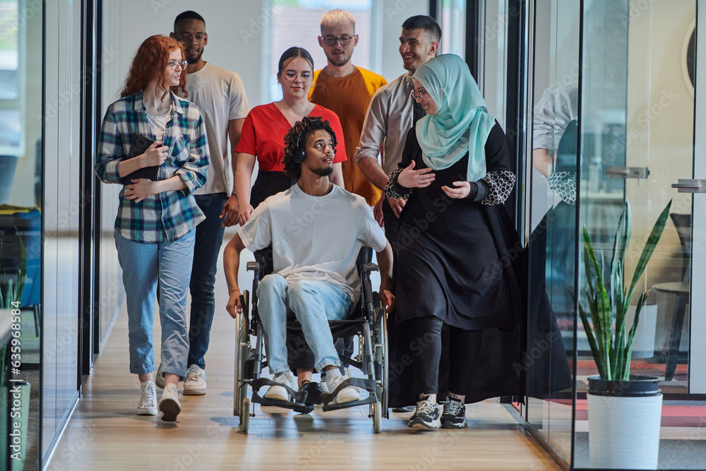 Fototapeta premium A diverse group of young business people walking a corridor in the glass-enclosed office of a modern startup, including a person in a wheelchair and a woman wearing a hijab, showing a dynamic mix of