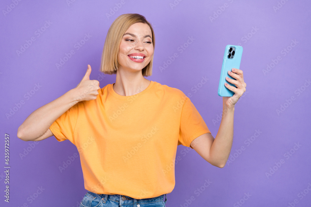 Portrait of satisfied cute girl dressed stylish clothes making selfie on smartphone show thumb up isolated on violet color background Portrait of satisfied cute girl dressed stylish clothes making selfie on smartphone show thumb up isolated on violet color background