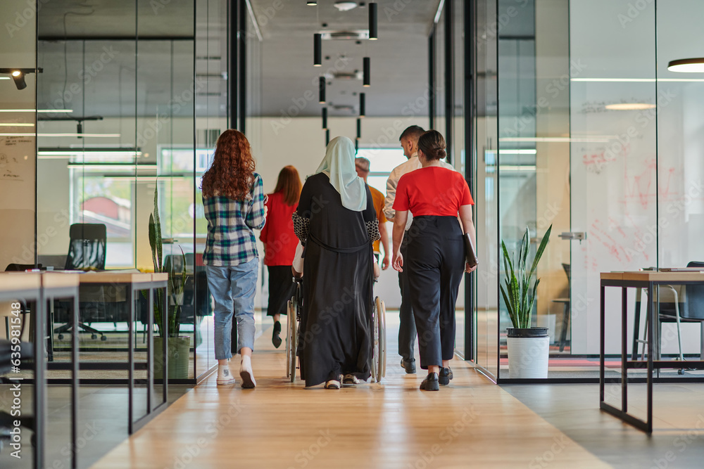 A diverse group of business people walking a corridor in the glass-enclosed office of a modern startup, including a person in a wheelchair and a woman wearing a hijab, showing a dynamic mix of