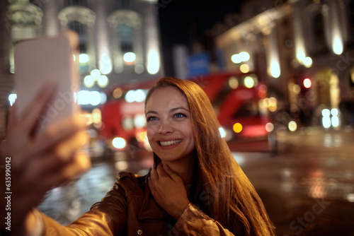 Young caucasian woman taking a selfie at the piccadilly circus in London UK at night