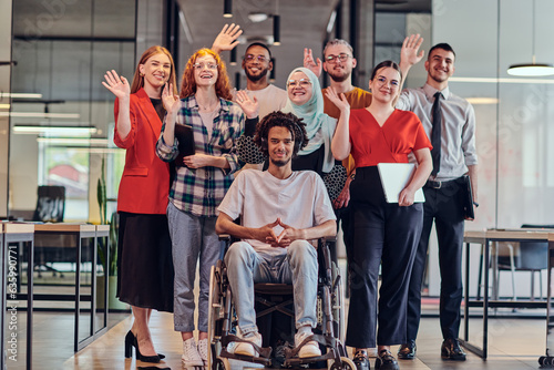 A diverse group of young business people congregates within a modern startup's glass-enclosed office, featuring inclusivity with a person in a wheelchair, an African American young man , and a hijab