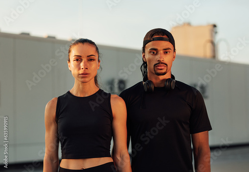 Portrait of two athletes in black sportswear standing together. Young athletes relaxing on the roof at sunset.