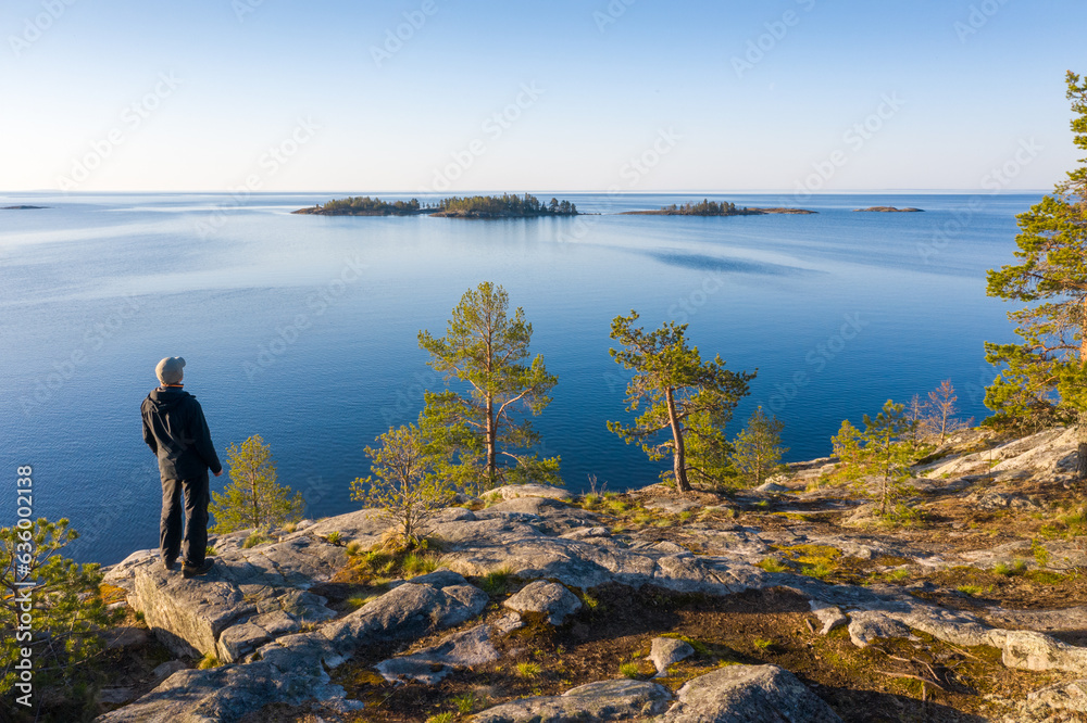 A man on a rocky island with pine trees looks into the sea. A man on a rocky island with pine trees looks into the sea.