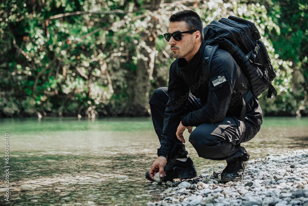 Mature man in a black military uniform stands in a relaxed pose at the edge of a river Mature man in a black military uniform stands in a relaxed pose at the edge of a river