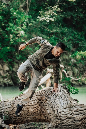 Man in a full military uniform leaps over a large tree trunk, executing a daring physical feat