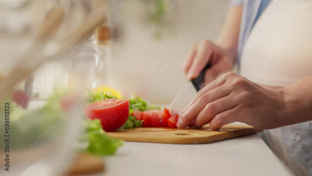 Pregnant, a young parent cuts a red-colored tomato in the kitchen of a private house. The expectant mother cuts fresh juicy tomato with a knife follows the modern principles of morning salads, morning Pregnant, a young parent cuts a red-colored tomato in the kitchen of a private house. The expectant mother cuts fresh juicy tomato with a knife follows the modern principles of morning salads, morning