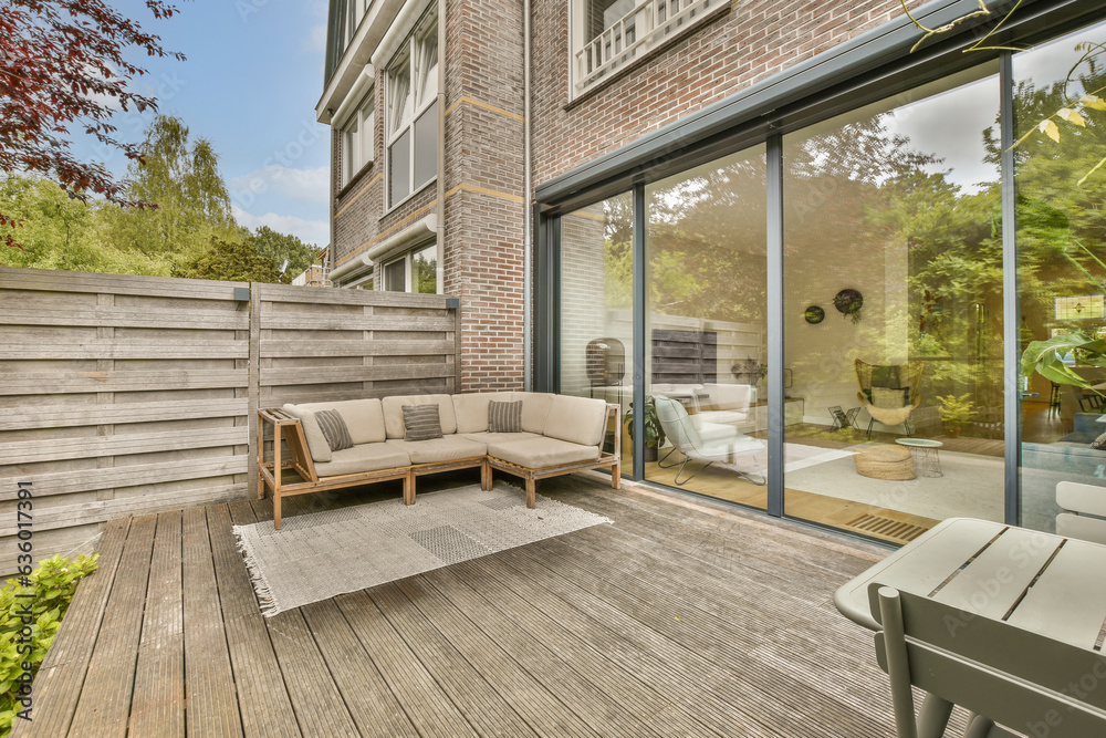 an outside living area with wood flooring and sliding glass doors leading to the decked back yard on a sunny day