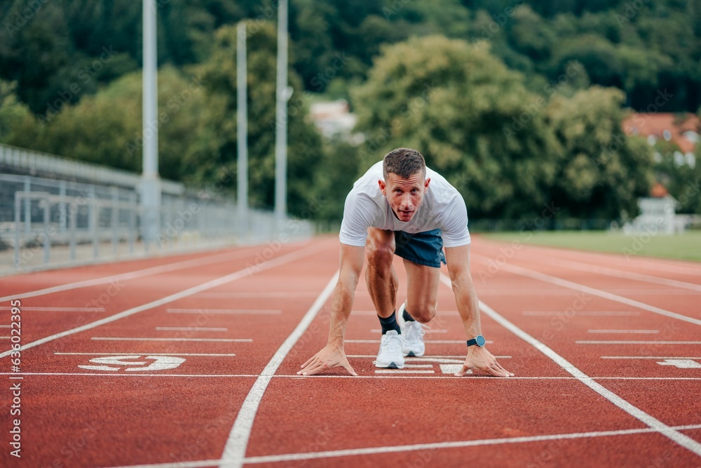 Young adult running on a track surrounded by lush, leafy trees in the background Young adult running on a track surrounded by lush, leafy trees in the background