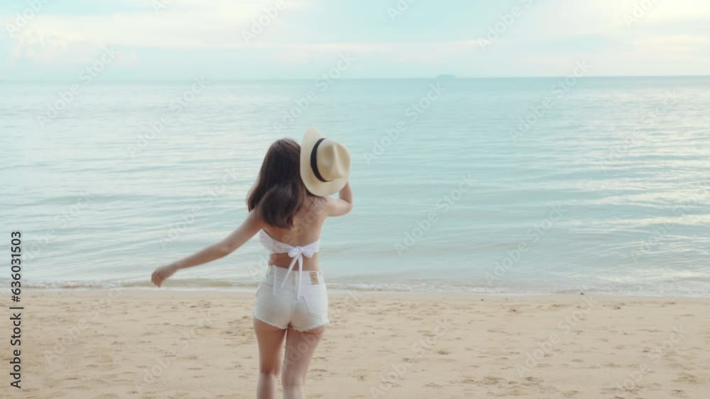 Beautiful Asian woman wear sungrass and hat turning back running to tropical paradise beach, Happy female in bikini having fun with hand to camera inviting you come with me
