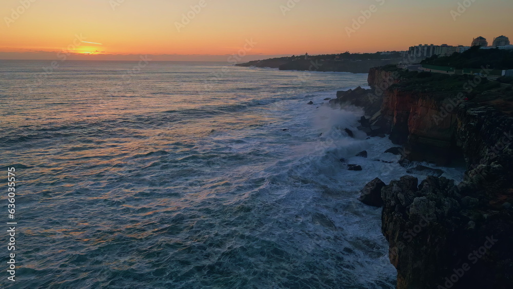 Beautiful calm coastal sunset over foamy ocean splashing on rocky shore aerial