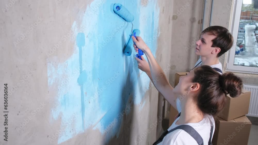 Couple in new home during repair works painting wall together. Happy family holding paint roller