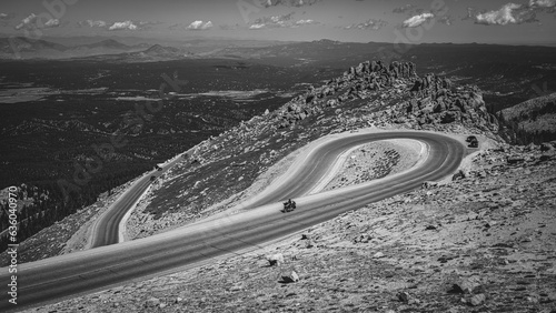 Solo motorcycle driving down a mountain road on a sunny day in grayscale