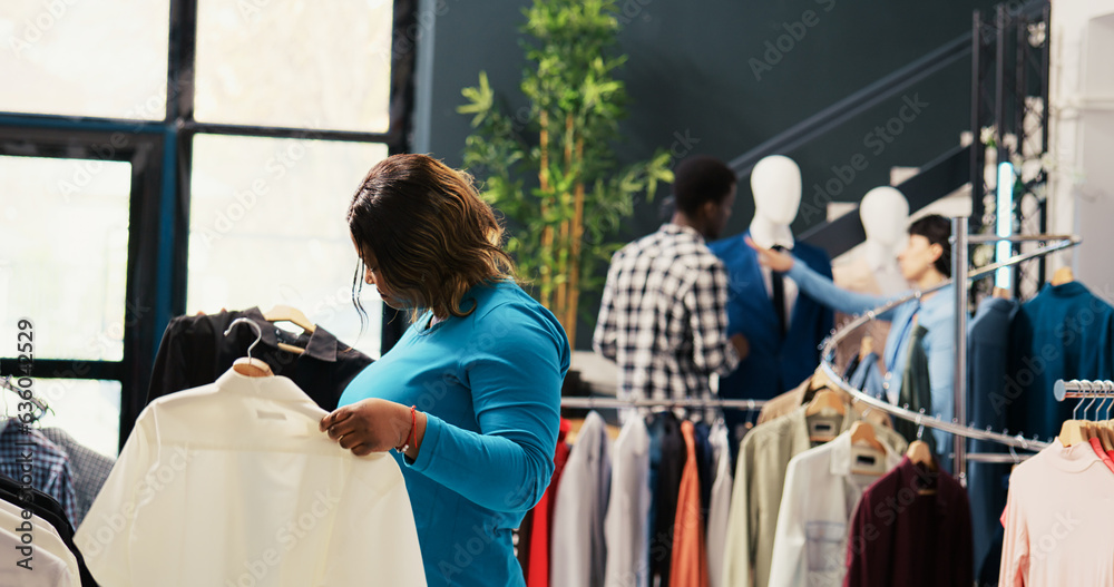African american customer looking at new fashion collection, shopping for fashionable clothes in modern boutique. Stylish client checking racks with trendy merchandise, analyzing fabric in store African american customer looking at new fashion collection, shopping for fashionable clothes in modern boutique. Stylish client checking racks with trendy merchandise, analyzing fabric in store