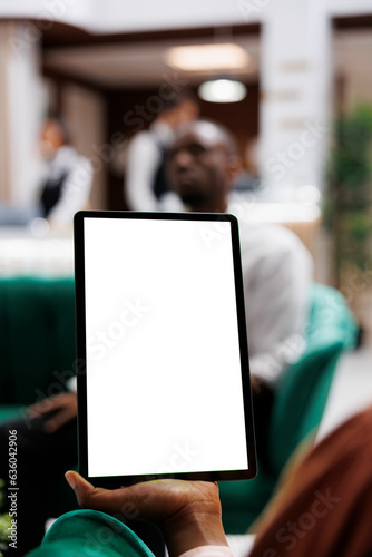Female person looking at white screen on digital tablet, using blank display with copyspace in lounge area at hotel lobby. Young adult holding device with isolated template. Close up.