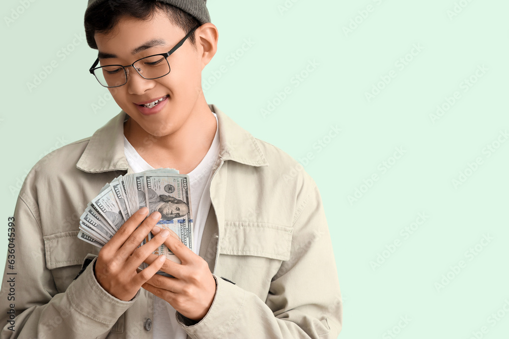 Young Asian man with dollar banknotes on green background, closeup Young Asian man with dollar banknotes on green background, closeup