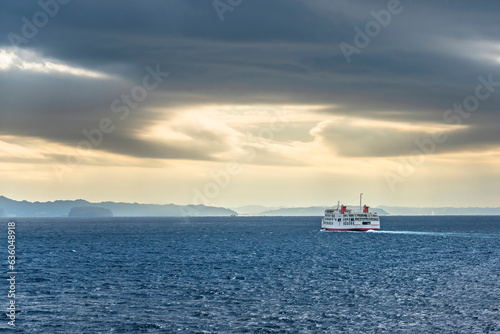 Ferry ship on the sea of the Uraga channel sailing towards the Kanaya port along the coasts of the Boso peninsula in the morning light below a stormy sky. photo