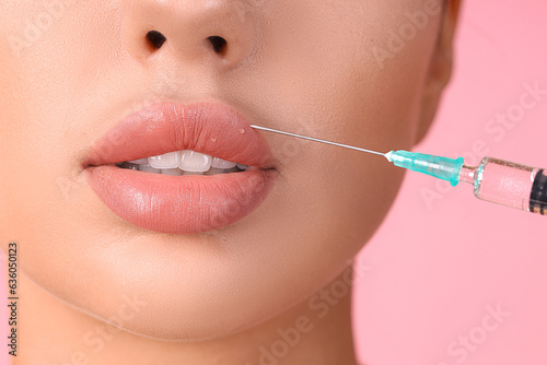 Young woman receiving lip injection on pink background, closeup