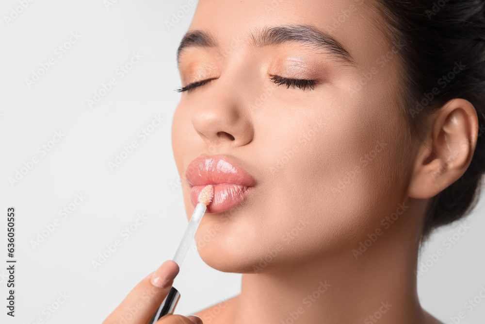 Young woman applying lipgloss on light background, closeup - obrazy, fototapety, plakaty 