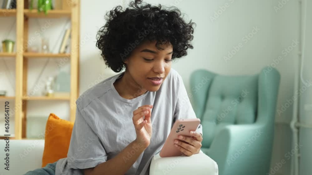 African girl holding smartphone touch screen typing scroll page at home. Woman with cell phone surfing internet using social media apps playing game. Shopping online Internet news cellphone addiction