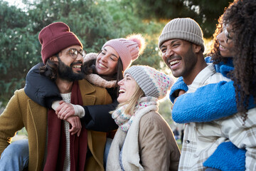 Cheerful group of smiling friends piggyback ride winter time outdoors. Young people have fun together in park on sunny day enjoying vacation party. Concept of friendship, relationships and happiness.