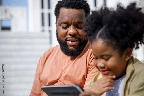 Dad watches his daughter learn on tablet photo