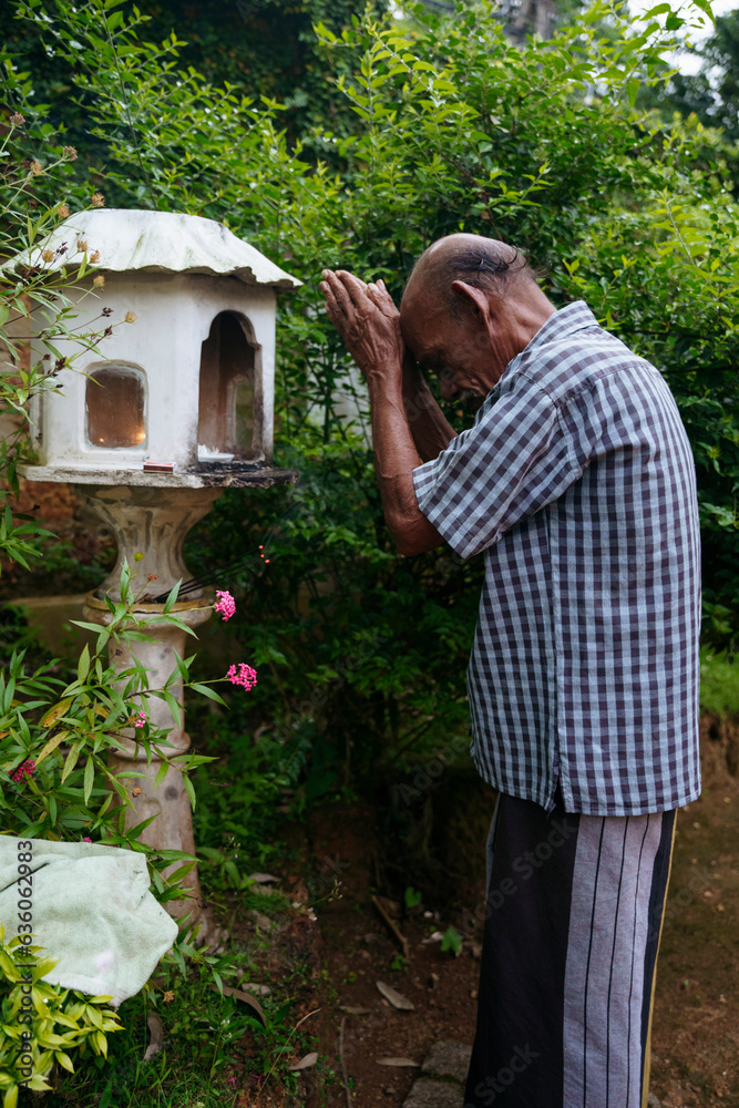 An elderly Buddhist prays in front of the altar An elderly Buddhist prays in front of the altar